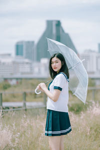 Portrait of young woman with umbrella standing amidst plants on field