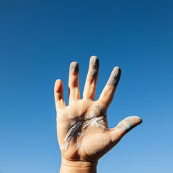 A woman's hand smeared with paint against a blue sky. close up