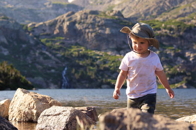 Rear view of boy standing on rock by water