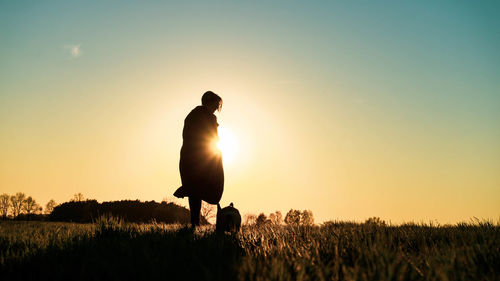 Woman with dog standing on field against sky during sunset