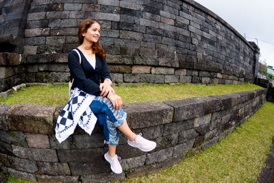 Full length woman sitting on the wall during the day at ceto temple tourist spot, solo.