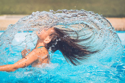 Side view of girl splashing water with hair in swimming pool