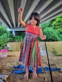 A girl holding a caught fish in front of a river.