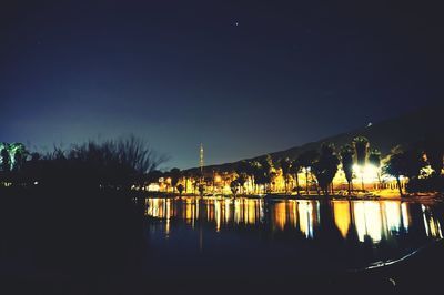 Illuminated buildings by river against sky at night