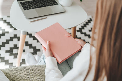 Close up of woman hands holding pink mockup notebook. freelance with laptop at home. copy space.