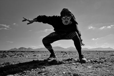 Full length of man crouching on ground against sky