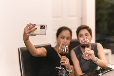 Two female friends drinking red wine and taking selfie on smart phone.