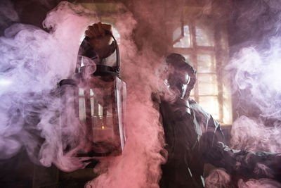 Woman holding oil lamp wearing gas mask standing amidst smoke