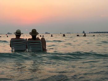 Rear view of couple sitting on chair at beach during sunset