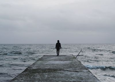 Rear view of man walking at sea against sky