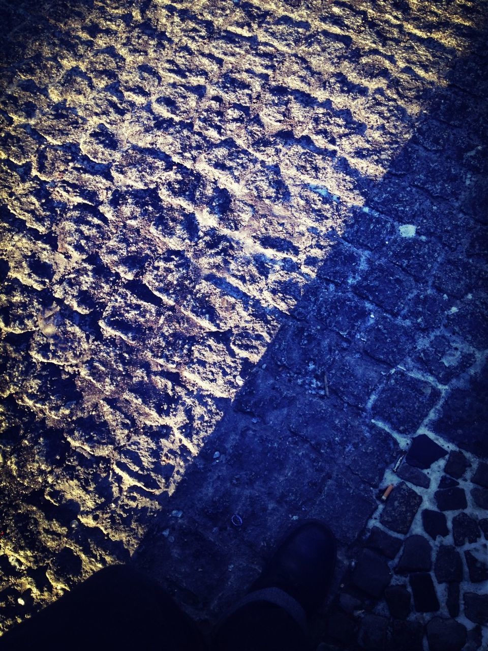 high angle view, textured, street, pattern, low section, asphalt, shadow, sunlight, person, day, beach, outdoors, cobblestone, shoe, footprint, water, close-up, puddle, paving stone, sand