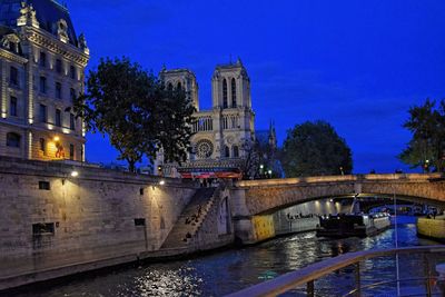 Illuminated bridge by river against blue sky at night