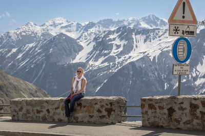 Woman sitting on retaining wall against snowcapped mountains