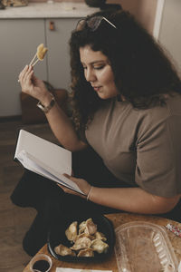 Businesswoman eating dumplings while reading diary at office