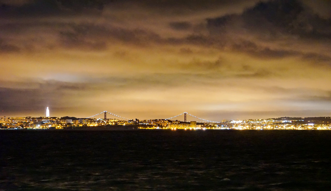 ILLUMINATED BUILDINGS BY SEA AGAINST SKY AT NIGHT