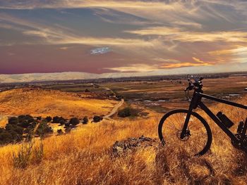 Bicycle on field against sky during sunset