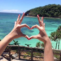Close-up of hands forming heart shape against blue sea