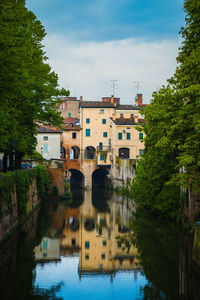 Arch bridge over river amidst buildings in city against sky