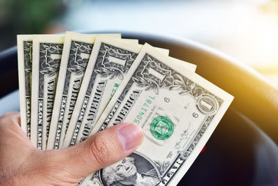 Cropped image of person holding paper currency against steering wheel of car
