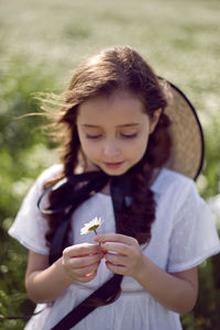 Portrait girl child in a white dress standing on a daisy field in a hat