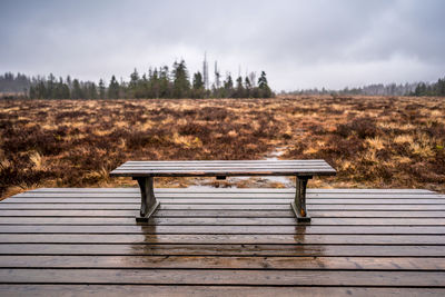 Empty bench on field against sky