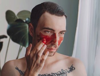 Close-up of shirtless young man applying face paint at home