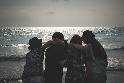 Rear view of friends with arms around standing at beach