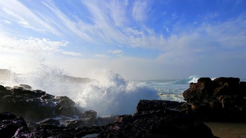 Sea waves splashing on rock against sky