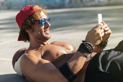 Shirtless man using smart phone while leaning on ball