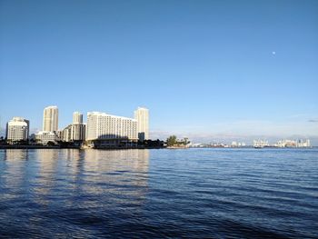 Sea by buildings against blue sky