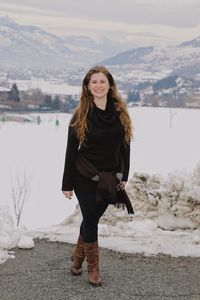 Portrait of smiling woman standing on road against snowcapped mountain