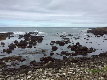 Scenic view of rocky beach against cloudy sky