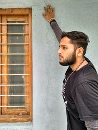 Side view of young man looking away against wall