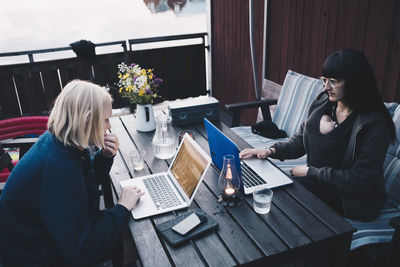 High angle view of female friends using laptop at wooden table in holiday villa