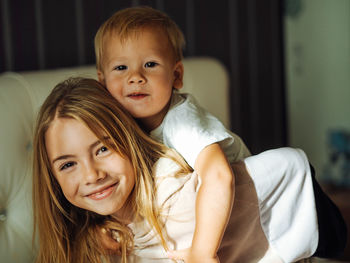 Portrait of cute sister carrying brother at home
