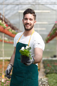 Portrait of smiling man holding plant in greenhouse
