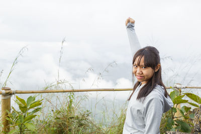 Portrait of smiling young woman standing by plants against sky