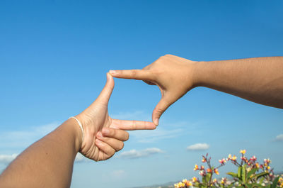 Close-up of hands joining fingers against blue sky