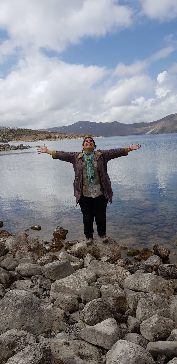 rock, water, one person, solid, rock - object, real people, standing, sky, lifestyles, beauty in nature, full length, leisure activity, scenics - nature, non-urban scene, cloud - sky, nature, casual clothing, lake, human arm, outdoors, arms raised