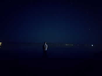 Rear view of man standing in sea against sky at night