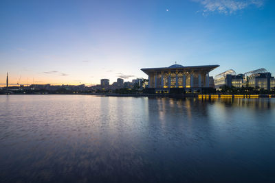 Illuminated building by lake against blue sky at dusk