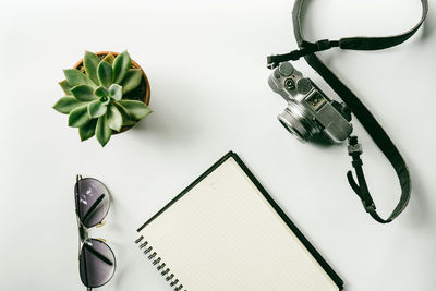 High angle view of camera with book and sunglasses on white background