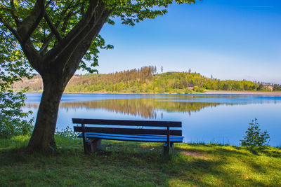 Empty bench by lake against blue sky