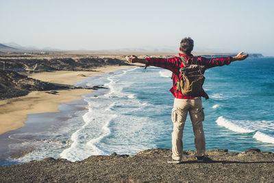 Full length rear view of man with arms outstretched standing at beach