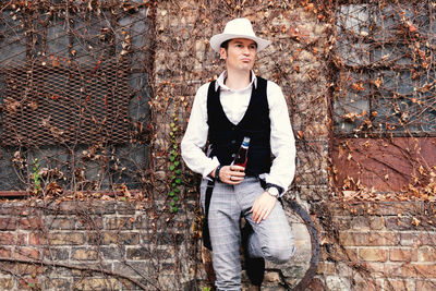 Portrait of retro-styled man drinking beer while leaning on a wall and thinking of something.