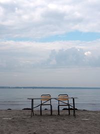 Chairs and table at beach against sky