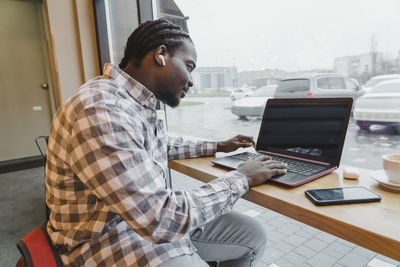 Young freelancer using laptop at table in cafe