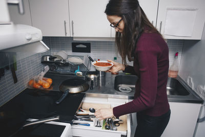 Side view of woman picking spoon from drawer in kitchen