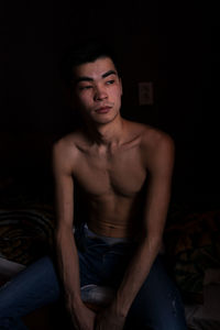 Portrait of shirtless young man sitting on bed