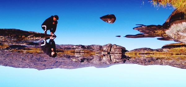 Low angle view of man standing on rock formation against clear blue sky